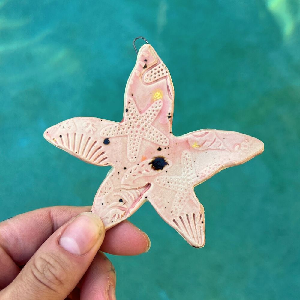 Pink starfish ornament held against a turquoise water background